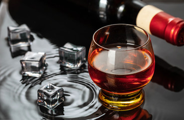 Bottle of red wine with wineglass. Water splash and droplet on the black reflection.