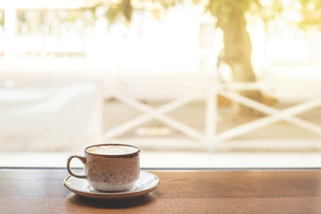 Rustic cup of cappuccino with saucer on a wooden table of a coffee shop by the window with bright sunlight. Copy space.