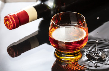 Bottle of red wine with wineglass. Water splash and droplet on the black reflection.