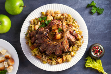 Crown roast of pork stuffed with apples and bread crumbs and celery sticks on white plate
