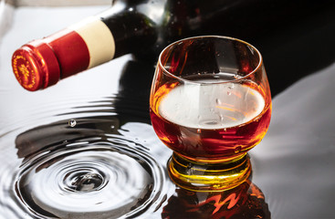 Bottle of red wine with wineglass. Water splash and droplet on the black reflection.