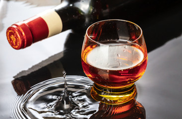 Bottle of red wine with wineglass. Water splash and droplet on the black reflection.