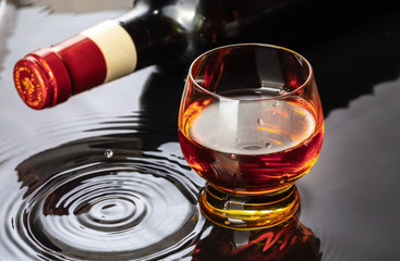 Bottle of red wine with wineglass. Water splash and droplet on the black reflection.