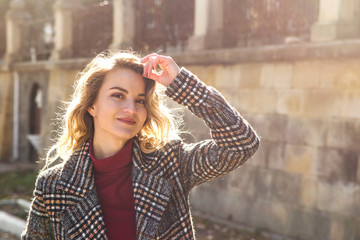 A young Caucasian girl in an autumn checkered coat walks around the city on a sunny day. Her hair backlit by light and looking to the camera.