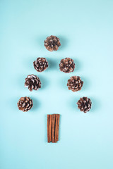 Cinnamon cones and sticks are laid out in the form of a minimalistic Christmas tree on a blue background. Creative flat lay, top view, copu space.