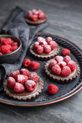 Cocoa crust tartlets filled with dark chocolate mousse made from whipped cream and raspberry puree, topped with fresh berries