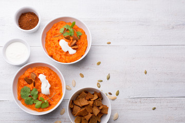 Pumpkin dish with croutons, sour cream, pumpkin seeds, cilantro and spices on a white wooden background