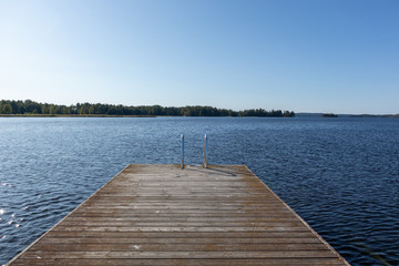 Wooden swimming dock pier with metal ladder on calm blue lake sunny day on nature finland idyllic...