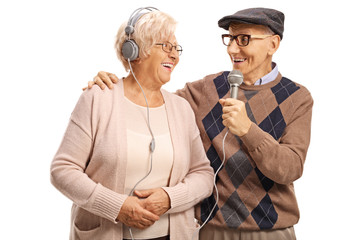 Elderly man singing on a microphone to an elderly woman with headphones