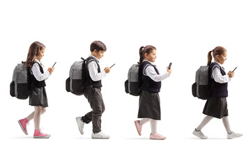 Obraz premium Three schoolgirls and one schoolboy with mobile phones walking in line