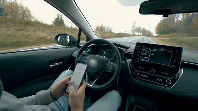 Driver types on a phone while a car goes on autopilot. Automatic, self-driving car.