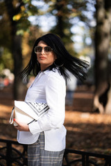 Obraz premium Autumn fashion outdoor. The girl in fashionable stylish white shirt , pants and sunglasses, autumnal lifestyle on the background of blurry yellow-green trees in the park. Vertical