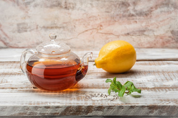 Fototapeta na wymiar tea food, on a wooden whitish table a glass teapot, a sprig of mint and lemon on the background of the wall