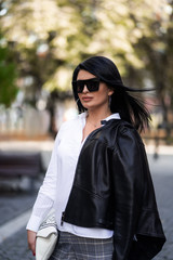 Autumn fashion outdoor. The girl in fashionable stylish white shirt , pants, jacket and sunglasses, autumnal lifestyle on the background of blurry yellow-green trees in the park. Vertical