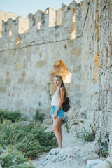 Fototapeta na wymiar Beautiful young blonde hair girl traveler near the fort wall Rhodes island, Greece