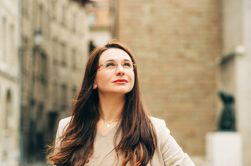 Outdoor portrait of beautiful woman posing on the city street, wearing beige suit and glasses