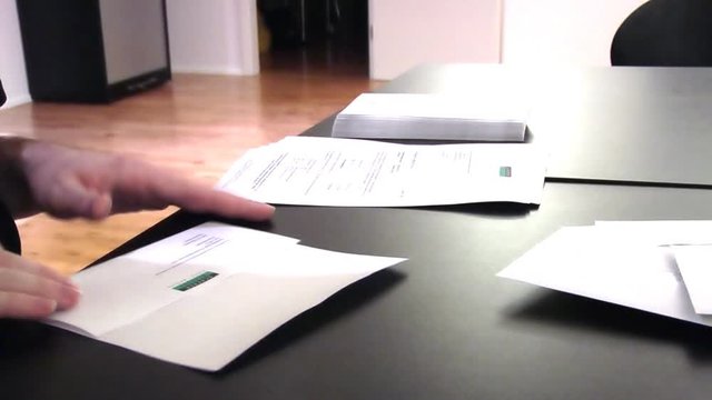 A man folding a stack of invoice letters and inserting them into envelops.