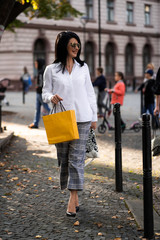 Autumn fashion outdoor. The girl in fashionable stylish white shirt , pants and sunglasses, autumnal lifestyle on the background of blurry yellow-green trees in the park. Vertical