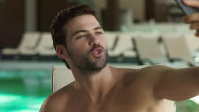 Portrait of sexy man posing for live video near pool. Funny guy in making selfie