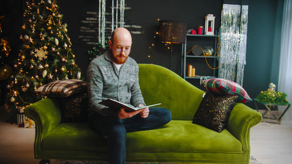 Serious with ginger beard with glasses reading a book in christmas set