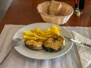 Two pieces of fried fish with potatoes in a plate on the table, rustic style