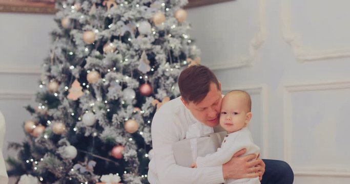 Kid gives dad a New Year's gift, dad is happy. Little son will take dad a box with a gift. Beautiful Christmas tree with toys, a cozy house.