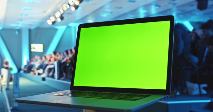 Modern blank green screen smartphone mobile with crowded evening conference hall and speaker on stage on background. Chroma key display. Tutorials seminars online. Automotive engineering technology