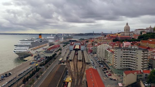 Aerial, pan, drone shot of large ships the Panteao national cruise harbor,, the Tejo river, the Santa Apolonia railway station and the cityscape of Lisbon city, in Portugal