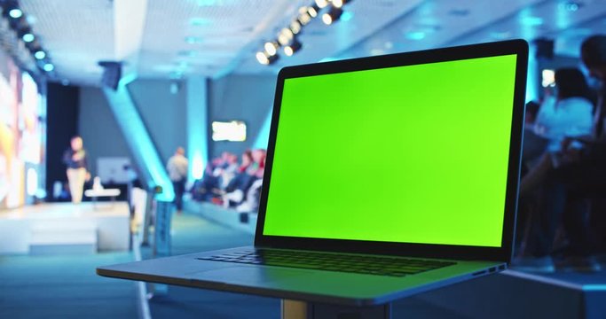 Chroma key laptop pc monitor in public space with people crowd listening to the coach speech on stage in conference meeting hall. Modern university education system. Green screen notebook mock-up.