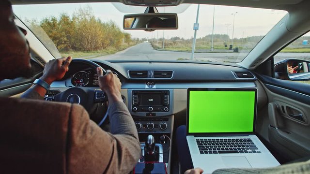 Successful afro-american man in business suit driving car to work. Inside car passenger using mock-up blank laptop greenscreen computer. Technology and people.
