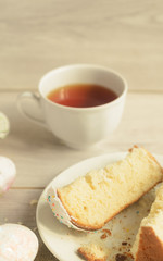 Holiday of Easter. Slices of sweet Easter cake, a cup of tea on a plate and Easter eggs on a light wooden background,copyspace on the top.