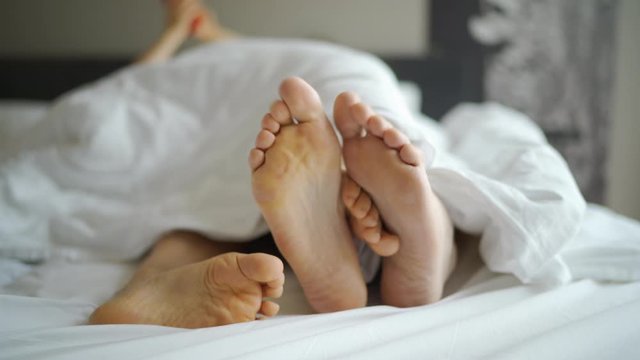 Shot of feet boyfriend and girlfriend lying in bed under blanket