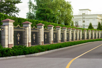 a stone fence with a rustik and an iron forged insert with a pattern and peaks near asphalt road...