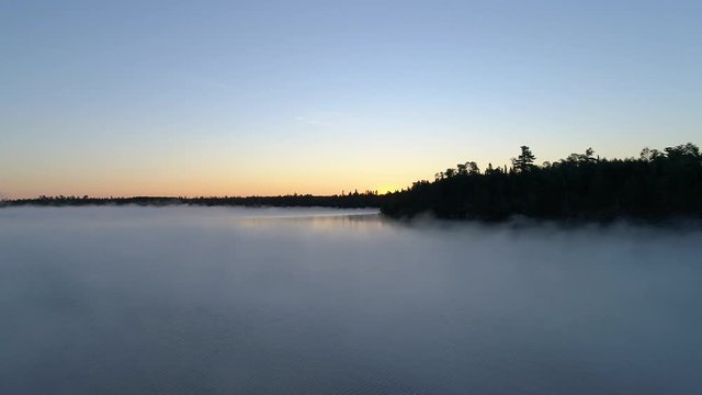 4K aerial reverse flight over a fog covered lake on a misty fall morning in Northwest Ontario, Canada.