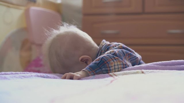 adorable little baby in checkered shirt nibbles plastic tube of medical nozzle suction at bed in light children room