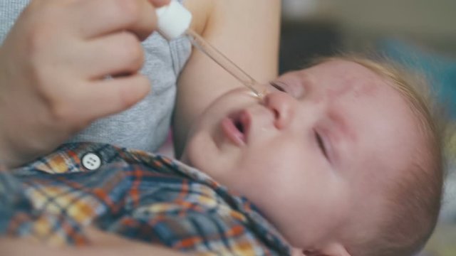 careful mommy gives cure from snuffle to little baby with glass pipette in light room on blurred background closeup