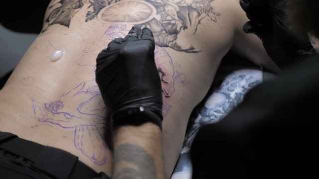 Professional tattoo artist showing the process of doing tattoo on back