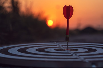 Close up red dart arrow hitting target center dartboard on sunset background. Business targeting...