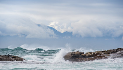 Sea landscape. Clouds sky, waves with splashes, mountains silhouettes. False bay. South Africa.