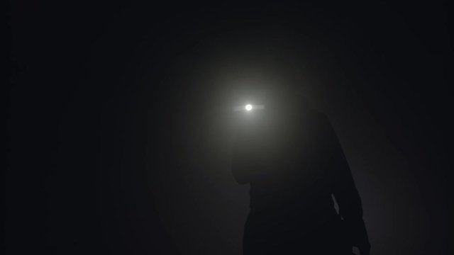 Close-up of man's silhouette with flashlight shining in the dark. Stock footage. Silhouette of man in thick fog