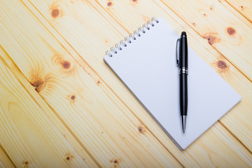 A memo paper notebook with black pen over wooden texture background, table blank space. Beginning of new goals and new year resolution concepts.
