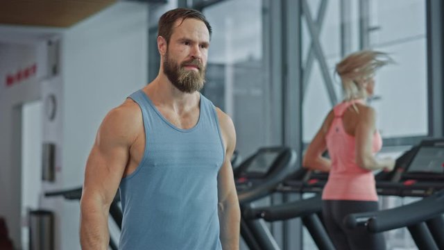 Muscular Heavyweight Champion Walks Through Gym, Drinks Protein Cocktail from Tumbler for Hydration and Muscle Mass. In the Background Sports People Running on Treadmills