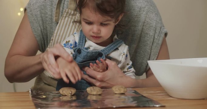 Cute toddler girl helping mom make cookies. Shot in 4K RAW on a cinema camera.