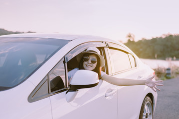 Happy asian woman wearing hat and sunglasses sitting in her car with sunset,Relaxing time,Positive thinking