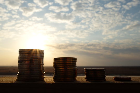 Decreasing stack of coins at sunset showing monetary loss concept 