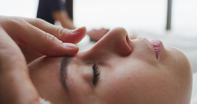 Close up of two young girlfriends with a towel on head are receiving a facial massage and spa treatment for perfect skin in a luxury wellness center.