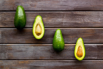 Avocado pattern - halfs of fruit - on dark wooden background top view copy space