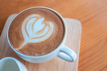 In the morning, Latte coffee cup with latte art on wooden table in coffee shop.