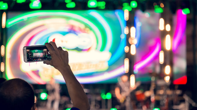 People use mobile phones to live or take pictures at concerts, with bright lights at night.