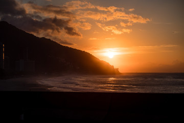 Orange sunset by the ocean in Sao Conrado, Rio de janeiro, with sun dipping behing a mountain. Am...